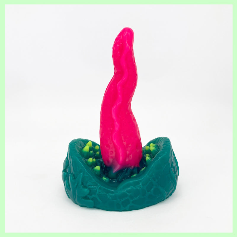 A venus fly trap inspired dildo with a green flower head, sharp looking teeth and a pink protruding tongue on a white background